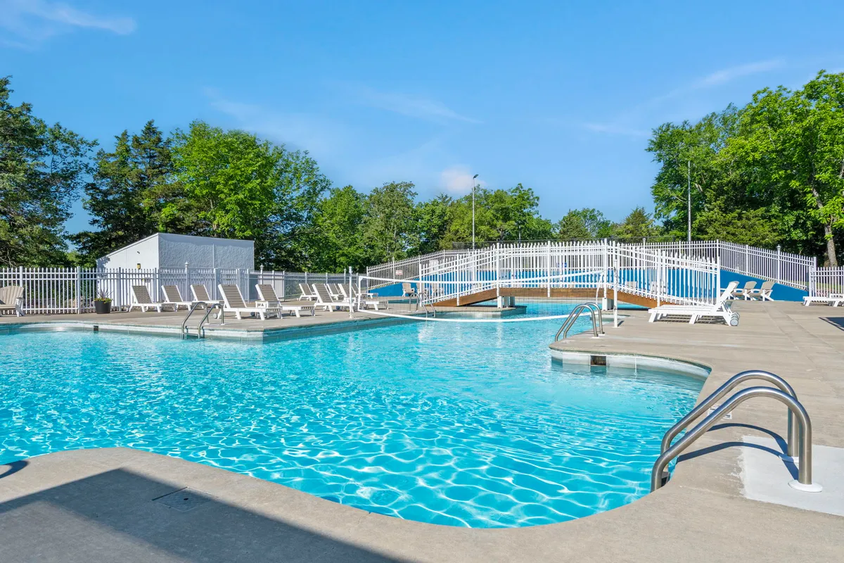 A sparkling swimming pool is the centerpiece, surrounded by comfortable lounge chairs and a charming bridge, all bathed in soft natural light. The setting exudes relaxation and is perfect for swimming, sunbathing, or social gatherings by the water.