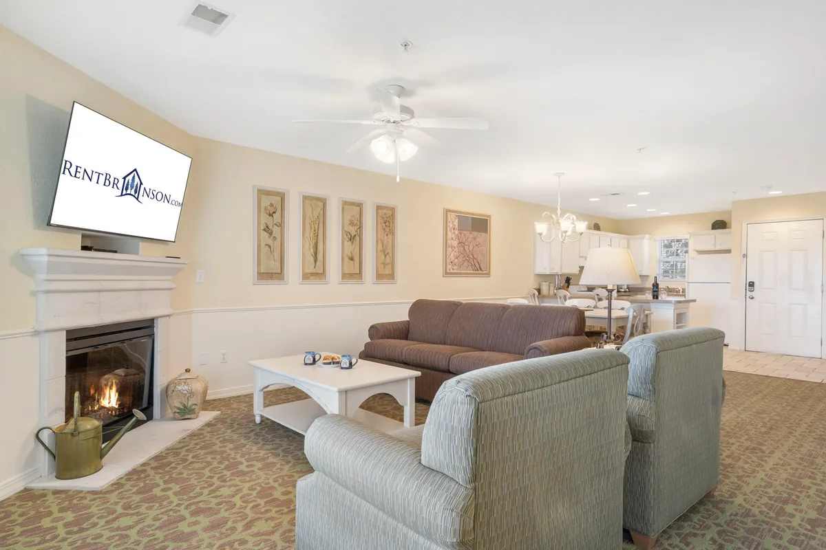 A comfortable living area is depicted, highlighting a central fireplace, a stylish seating arrangement, and a television above the hearth. The focus on the fireplace suggests warmth, making it easy to imagine unwinding after a day outdoors or hosting a movie night with loved ones.