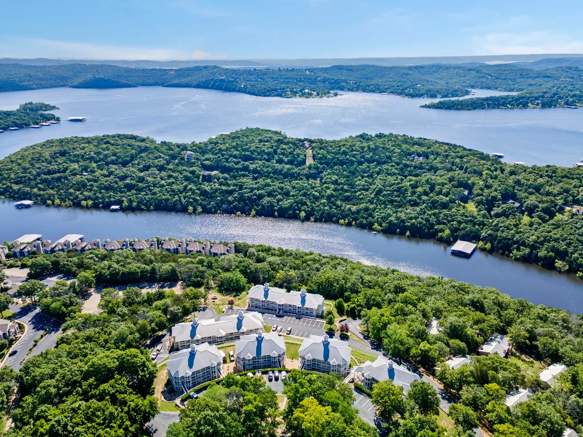 A sweeping view of a tranquil lake, bordered by lush greenery and a cluster of buildings nestled among the hills. The water is calm, inviting activities like boating and fishing, and the scene exudes a peaceful, nature-rich atmosphere.