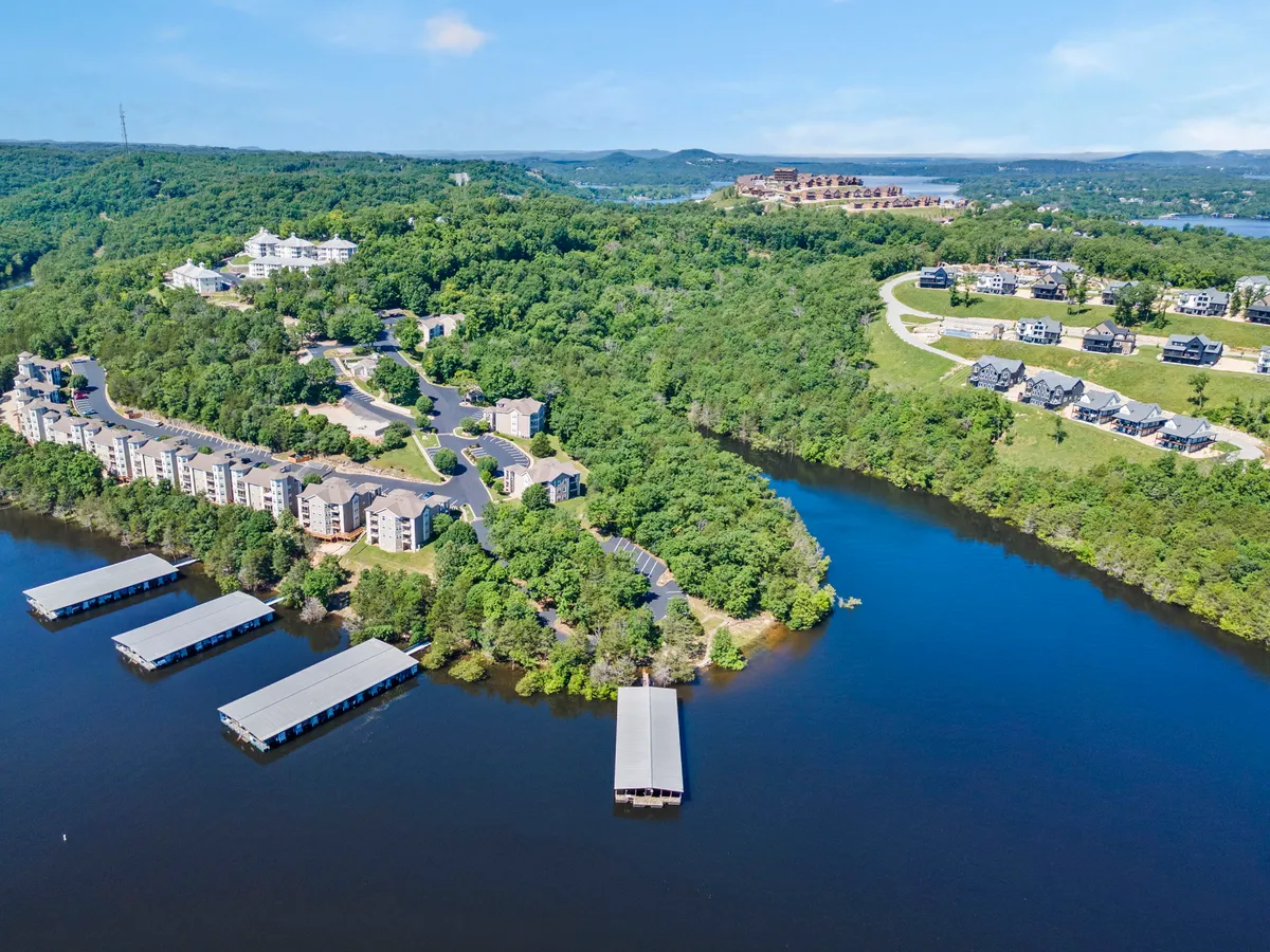 A tranquil waterfront scene with residential buildings overlooking a docking area and natural landscape. The calm water and greenery promote a sense of peace and easy access to outdoor activities like hiking and nature walks.