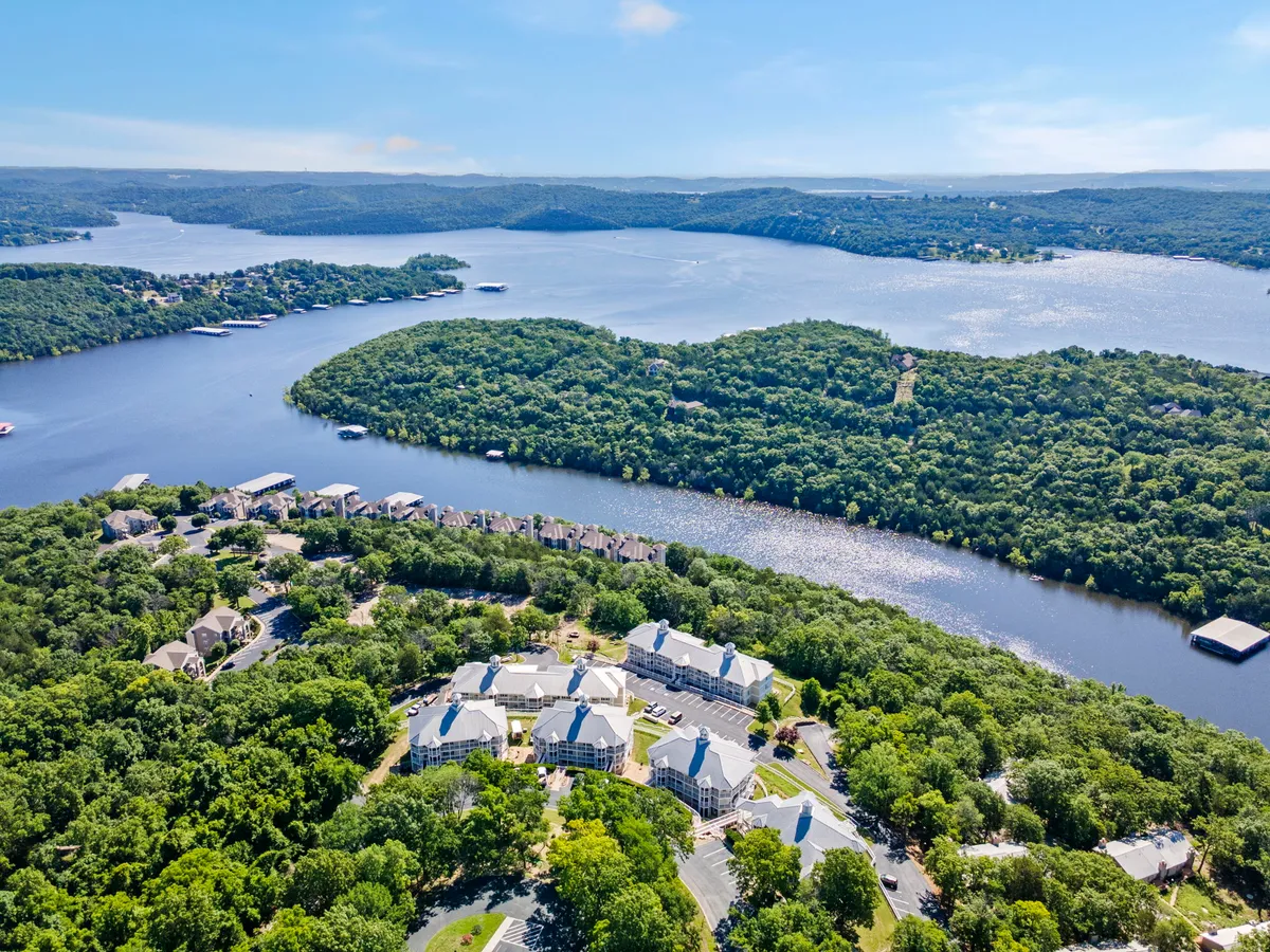 A picturesque scene featuring a lush green landscape bordering a sparkling lake, framed by modern residential buildings in the background. The setting exudes invitation for outdoor activities such as walking, boating, and picnicking.