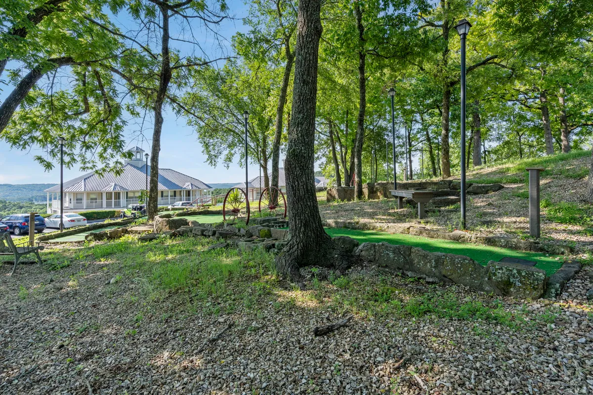 A beautifully landscaped miniature golf area surrounded by vibrant greenery, stone walls, and several seating areas, all set against a scenic natural backdrop. The space is lively yet relaxed, ideal for families and social gatherings.