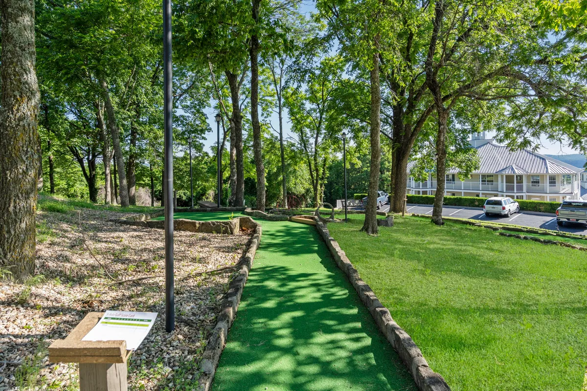 This image features a playful mini-golf course winding through lush greenery, bordered by a walking path. The inviting outdoor setting is ideal for families and groups to engage in friendly competition and enjoy the beauty of nature together.
