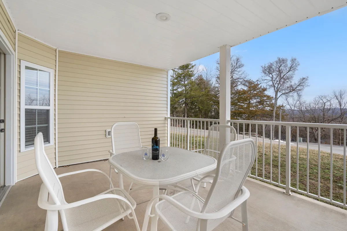 A serene deck area with a table set for two, complete with a wine bottle and chairs. The deck overlooks a beautiful landscape, providing direct outdoor access and an inviting spot to relax. The railing ensures safety for pets and small children, and the open view hints at nearby trails and resort amenities.