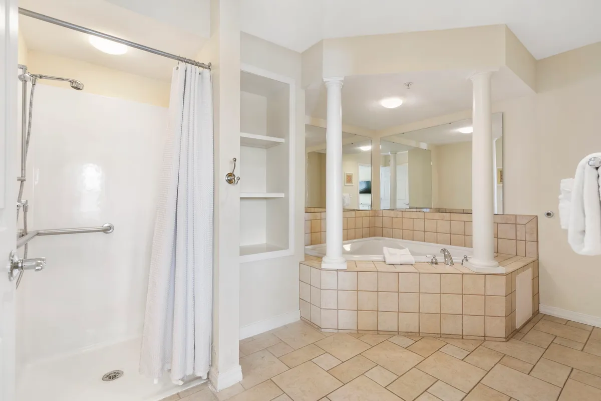 A tranquil ensuite bathroom is shown here, with a luxurious bathtub set between elegant pillars and a mirrored wall. The space is styled for relaxation, offering both a bathtub and shower area for a spa-like experience.
